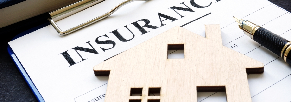 Home insurance paper policy and a wooden model of a house on top of it.