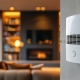 a close-up on a white carbon monoxide detector mounted high on the wall near the ceiling. in the blurry background, a cozy, modern family living room at dusk. The room is warm and inviting, featuring a comfortable sofa, a small bookshelf, and a fireplace in the background. Natural light filters in through a nearby window, creating a peaceful ambiance.